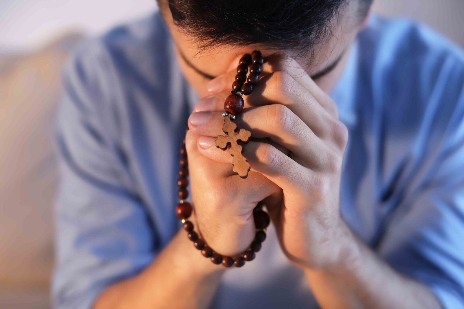 Religious young man with rosary beads praying at home, closeup